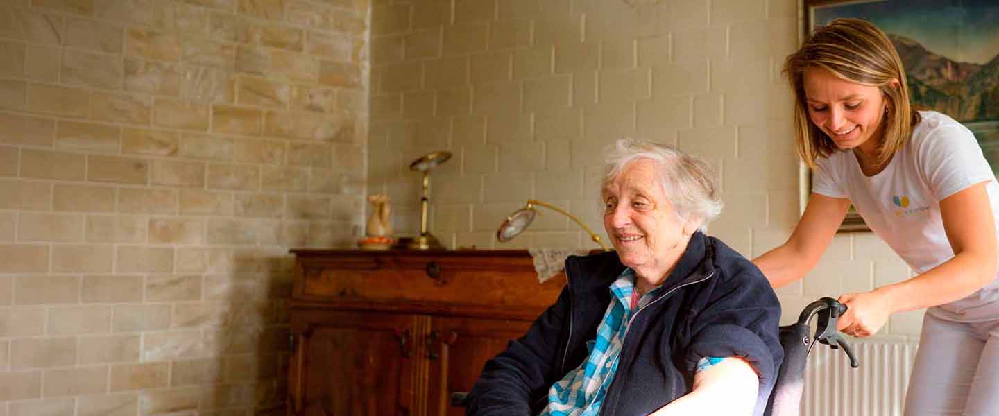 Pflegekraft von Miteinander unterstützt eine lächelnde Seniorin in ihrer Wohnung