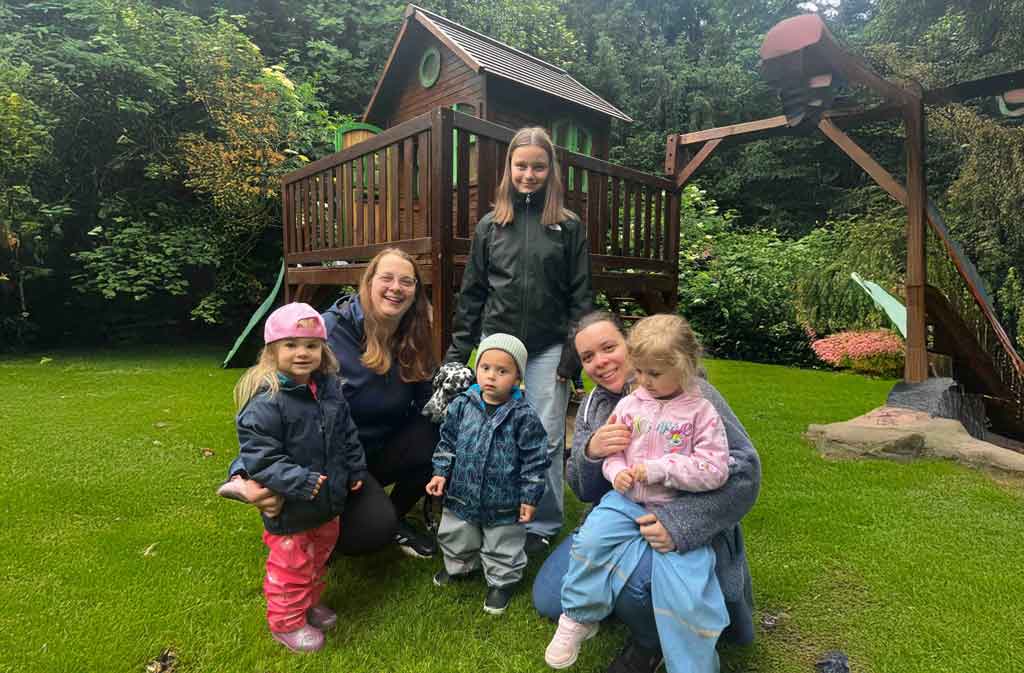 Zwei Betreuerinnen mit vier Kindern vor einem Spielhaus im Garten